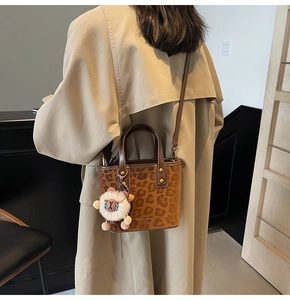 Detail of leopard print bucket bag with plush sheep charm and gold hardware on trench coat