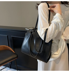 Close-up of black leather tote bag worn as an underarm shoulder bag with gold hardware