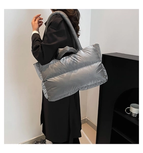 Silver quilted puffer tote bag shown on shoulder in a modern minimalist interior setting