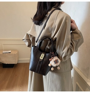 Detail of dark brown leather bucket bag with plush sheep charm and metallic clasp