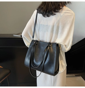 Model wearing a large black matte leather tote bag with dual handles for daily commute