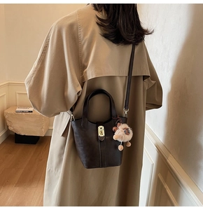 Detail of dark brown leather bucket bag with gold hardware and plush bear charm on a model