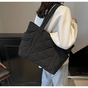 Detail of black quilted tote bag showing side zipper pocket and padded shoulder strap