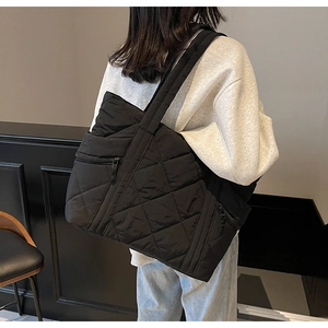 Detailed back view of a woman wearing a black quilted nylon tote bag with a wide shoulder strap