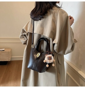 Detailed view of coffee leather bucket bag with gold lock and lion charm on model