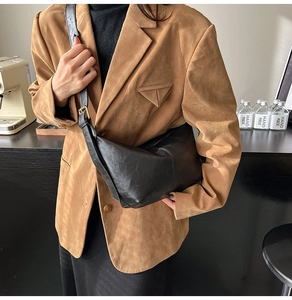 Minimalist black leather crescent bag with adjustable strap worn on brown blazer coat
