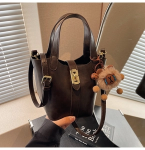Detail of a dark brown bucket bag with gold clasp and a plush sheep pendant