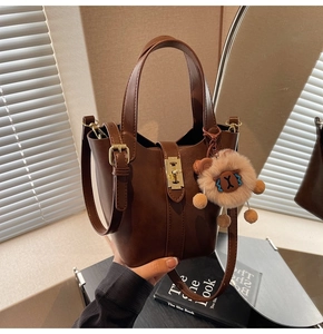 Detail of dark brown leather bucket bag with gold hardware and plush lion charm