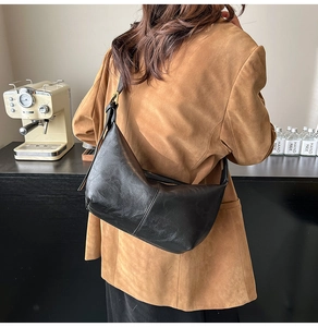 Detail of black pebbled leather half-moon shoulder bag with adjustable strap on model