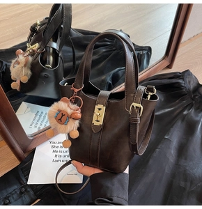 Detail of dark brown bucket bag with gold clasp and cute plush animal keychain