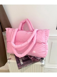 Pink glossy puffy tote bag with quilted padding and dual straps on white suitcase
