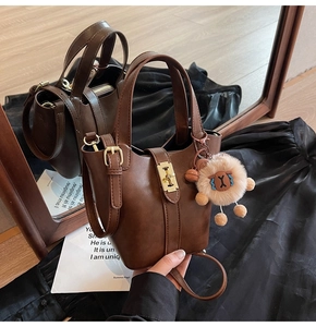 Detail of dark brown leather bucket bag with gold clasp and plush lamb charm accessory