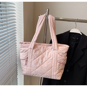 Detail of light pink quilted tote bag showing rhombus texture and dual side zipper pockets