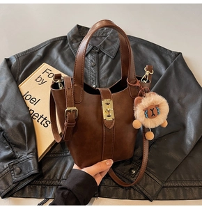 Detailed view of brown bucket bag with gold lock, lion charm, and leather strap