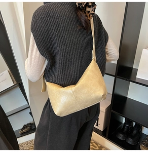 Close-up of a cream pleated leather crescent bag worn by a model in a minimal setting