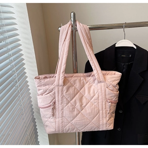 Detailed view of light pink quilted tote bag with side zippers hanging on a metal rack