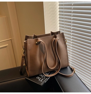 Close-up of a textured brown tote bag with adjustable shoulder strap and gusset detail