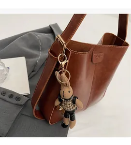 Close-up of brown leather bucket bag with brand embossing and knit bunny charm