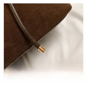 Detail of dark brown suede tote bag featuring slim leather cord with gold metal hardware