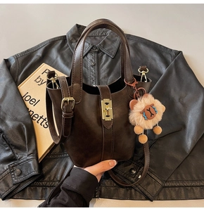 Detailed view of a brown bucket bag with gold hardware lock and fuzzy animal charm