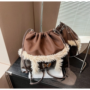 Detail of a brown leather drawstring bag with white faux fur trim and silver butterfly charm