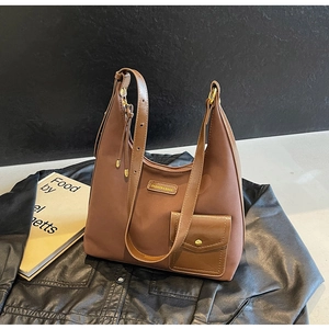 Detail of a brown large capacity hobo bag with metal logo and leather side pocket