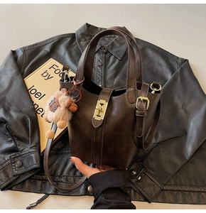 Detail of deep brown bucket bag with metal buckle and plush lion pendant accessory