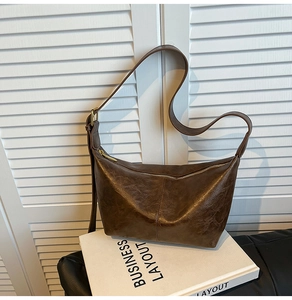 Detail of dark brown crescent hobo bag with vintage pleats and gold zipper on a book