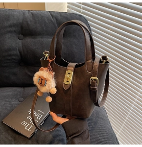 Detail of dark brown bucket bag with gold twist lock and plush lion charm on a sofa