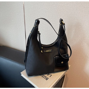 Detail of black crescent hobo bag featuring a metal logo and magnetic front pocket