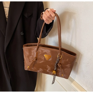Détail d'un sac cabas en cuir verni marron avec logo triangulaire doré et pompon