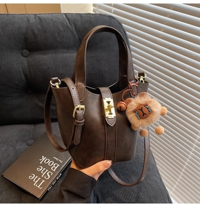 Detail of dark brown bucket bag with gold clasp and cute lion plush charm accessory