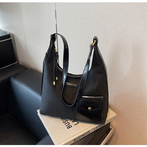 Detail of black nylon tote with leather trim and gold metal logo plaque showing premium texture