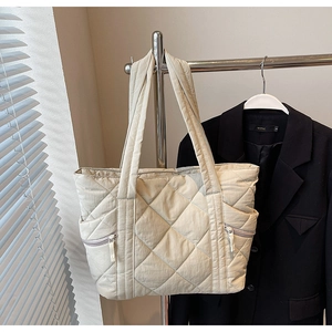 Detail of beige quilted tote bag featuring puffer texture and front zipper pockets