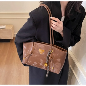 Détail d'un cabas en cuir verni marron avec plaque dorée et porte-clés tressé élégant