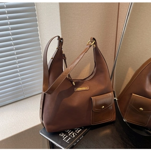 Detail of a brown hobo bag with a gold buckle pocket and polished metal brand plaque