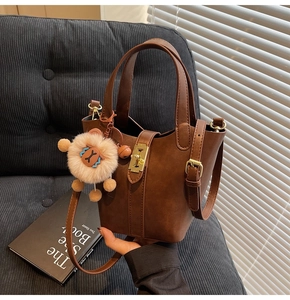 Detail of dark brown matte leather bucket bag featuring gold buckle and cute bear charm