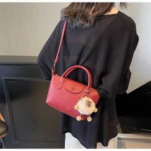 Detail of red pebbled leather tote with button flap and a cute beige sheep charm accessory