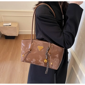 Détail du sac cabas en cuir marron brillant avec logo triangle doré et pompon tressé