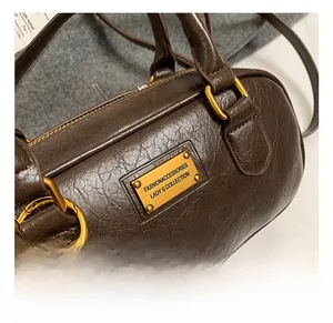 Detail of dark brown leather Boston bag showing gold hardware and logo plate textures