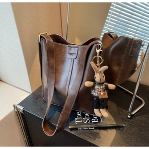 Detail of dark brown leather bucket bag with embossed logo and rabbit charm accessory