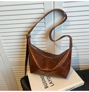 Detail of dark brown matte leather crescent bag with gold zipper and adjustable strap
