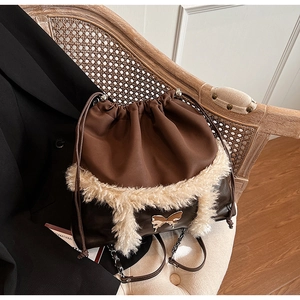 Detail of faux fur drawstring bucket bag with golden butterfly charm on a wooden chair