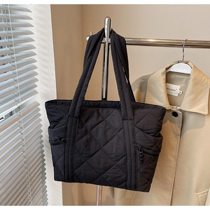 Close-up of black quilted nylon tote bag featuring side zipper pockets and diamond pattern