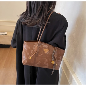 Détail d'un sac à bandoulière en cuir verni marron brillant avec emblème triangulaire