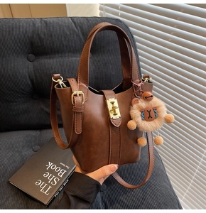 Brown leather bucket bag with gold buckle and cute sheep pendant on a sofa background