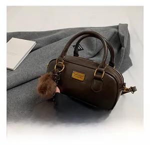 Detail of deep brown Boston bag with glossy texture, gold hardware, and fur charm accessory