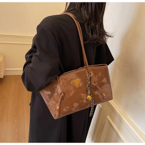 Détail du sac à bandoulière marron brillant avec logo triangle en métal et pendentif
