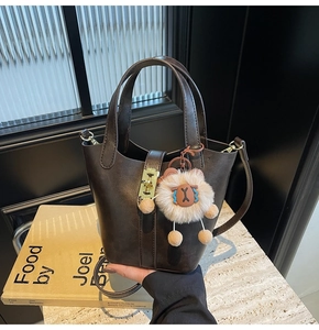 Detail of dark brown bucket bag featuring gold buckle and cute sheep plush charm accessory