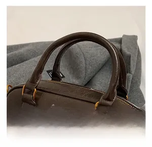 Detail view of smooth dual handles and golden hardware on dark brown leather boston bag